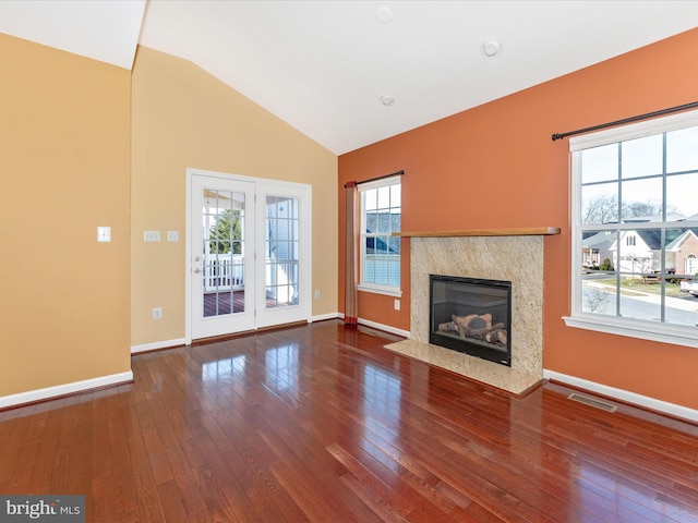 unfurnished living room with vaulted ceiling, a healthy amount of sunlight, a premium fireplace, and hardwood / wood-style floors