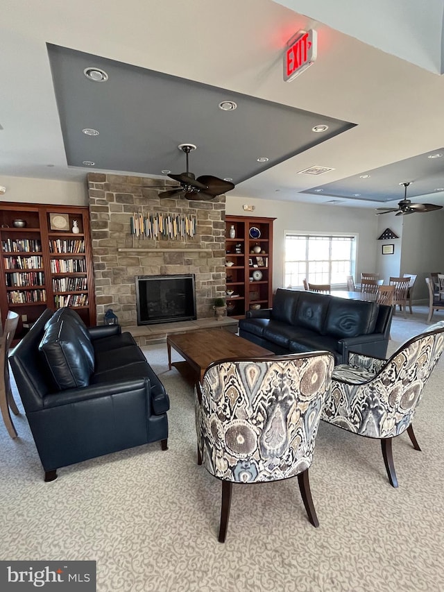 carpeted living room with a large fireplace, built in features, ceiling fan, and a tray ceiling