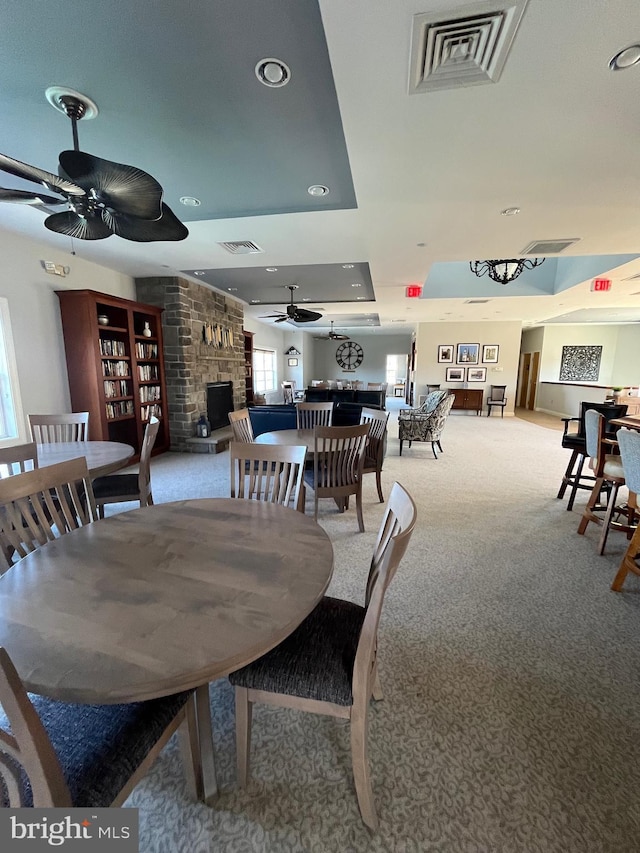 carpeted dining area with a large fireplace and ceiling fan