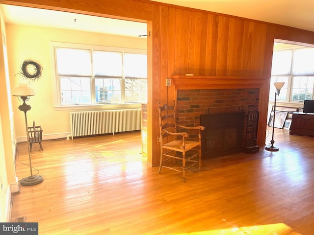 living room featuring wood-type flooring, radiator, a brick fireplace, and wood walls