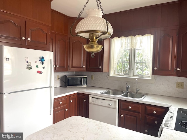 kitchen with pendant lighting, white appliances, sink, and backsplash