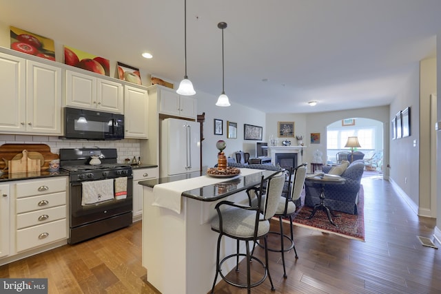 kitchen with a breakfast bar, pendant lighting, white cabinetry, backsplash, and black appliances