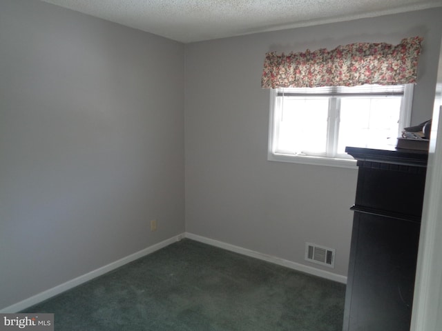 spare room featuring dark colored carpet and a textured ceiling