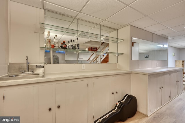 bar featuring sink, a drop ceiling, and light hardwood / wood-style flooring