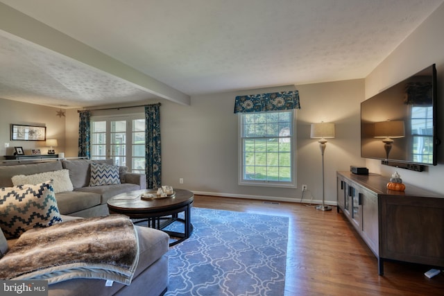 living room featuring beamed ceiling, wood-type flooring, and a textured ceiling