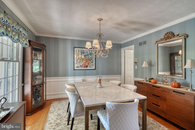 dining space featuring crown molding, a textured ceiling, an inviting chandelier, and light hardwood / wood-style flooring