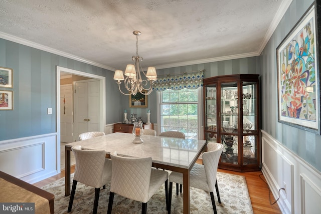 dining space featuring ornamental molding, a chandelier, a textured ceiling, and light wood-type flooring