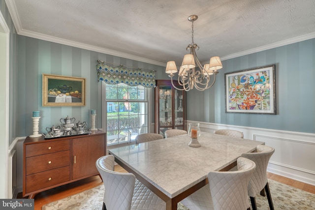 dining space with a notable chandelier, light hardwood / wood-style flooring, ornamental molding, and a textured ceiling