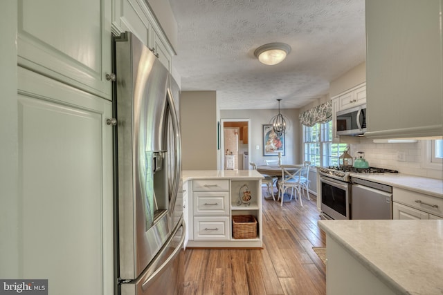 kitchen featuring light hardwood / wood-style flooring, pendant lighting, stainless steel appliances, decorative backsplash, and white cabinets