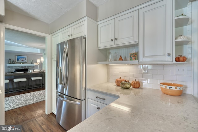 kitchen featuring backsplash, dark hardwood / wood-style floors, light stone countertops, white cabinets, and stainless steel fridge with ice dispenser