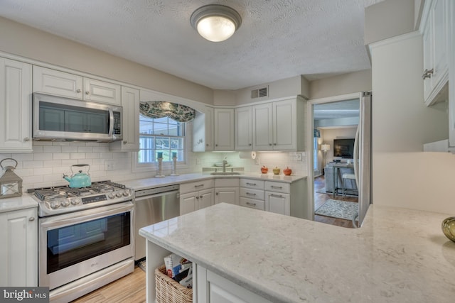 kitchen with white cabinetry, appliances with stainless steel finishes, backsplash, and light hardwood / wood-style floors