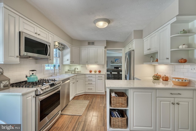 kitchen with sink, tasteful backsplash, appliances with stainless steel finishes, light hardwood / wood-style floors, and white cabinets