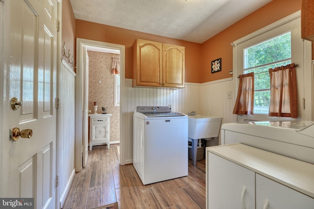 laundry room featuring sink, cabinets, a textured ceiling, washer / clothes dryer, and light hardwood / wood-style floors