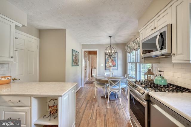 kitchen with an inviting chandelier, stainless steel appliances, wood-type flooring, white cabinets, and decorative light fixtures