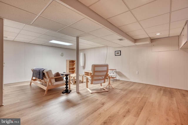 living area with a paneled ceiling and light wood-type flooring