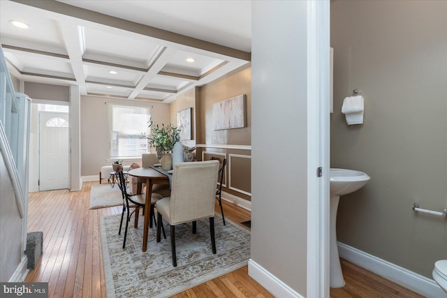 dining area featuring beamed ceiling, coffered ceiling, and light hardwood / wood-style flooring