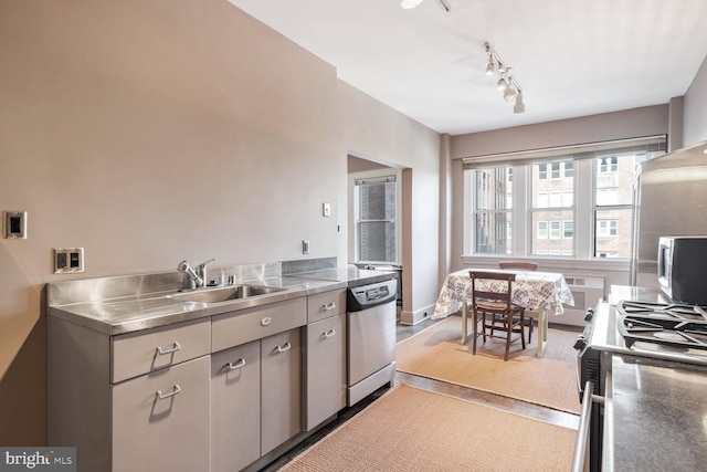 kitchen with sink, hardwood / wood-style flooring, rail lighting, stainless steel counters, and appliances with stainless steel finishes