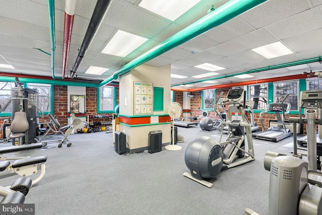 exercise room featuring brick wall and a drop ceiling