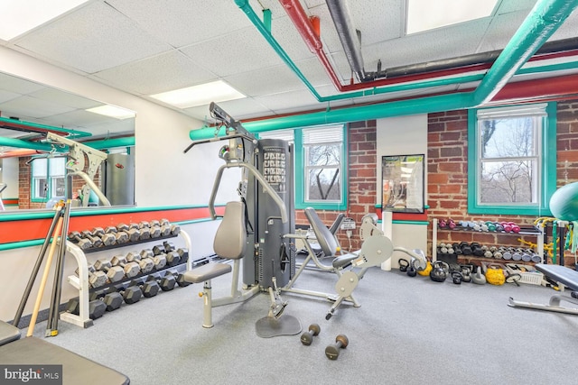 workout area with brick wall and a drop ceiling