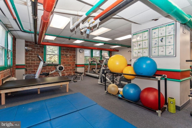 exercise room featuring a drop ceiling and brick wall