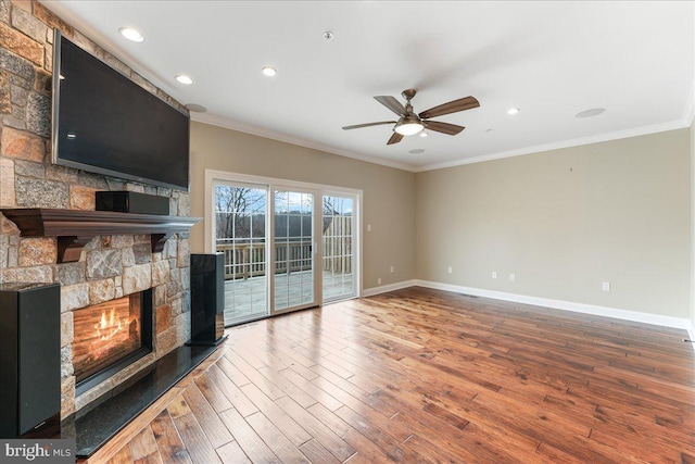 unfurnished living room featuring a stone fireplace, wood-type flooring, ornamental molding, and ceiling fan