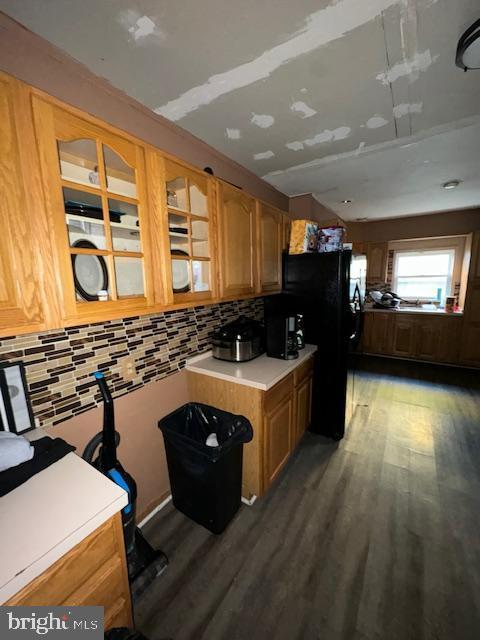 kitchen with black refrigerator, backsplash, and dark wood-type flooring