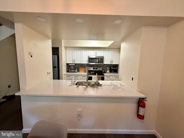 kitchen featuring white cabinetry, tasteful backsplash, appliances with stainless steel finishes, kitchen peninsula, and light stone countertops