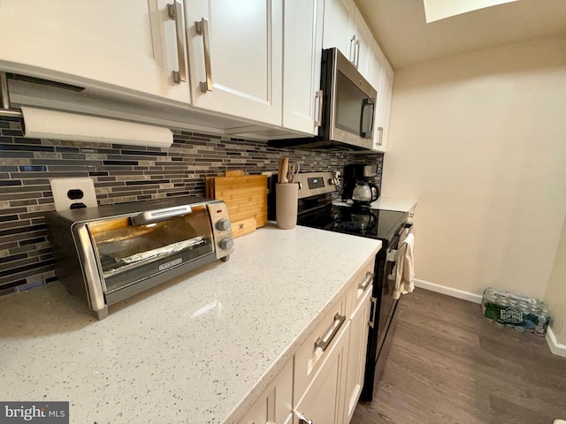 kitchen featuring dark wood-type flooring, white cabinetry, stainless steel appliances, light stone countertops, and backsplash