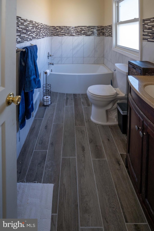 bathroom with vanity, a tub to relax in, tile walls, and toilet