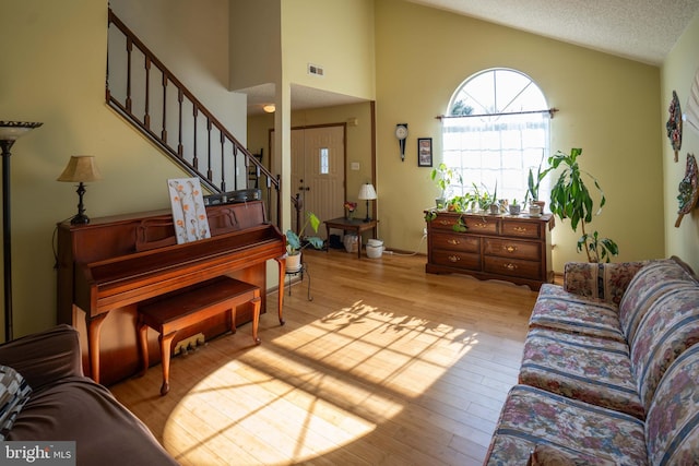 living room featuring high vaulted ceiling, a textured ceiling, and light hardwood / wood-style flooring