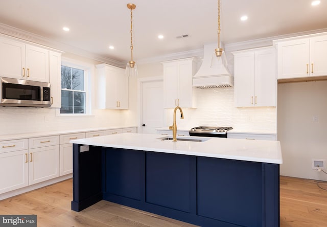 kitchen featuring an island with sink, sink, white cabinets, hanging light fixtures, and stainless steel appliances