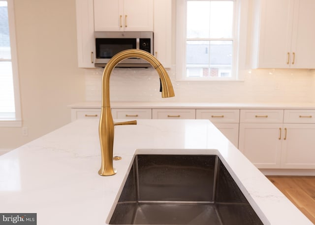 details featuring sink, white cabinets, light stone counters, and decorative backsplash