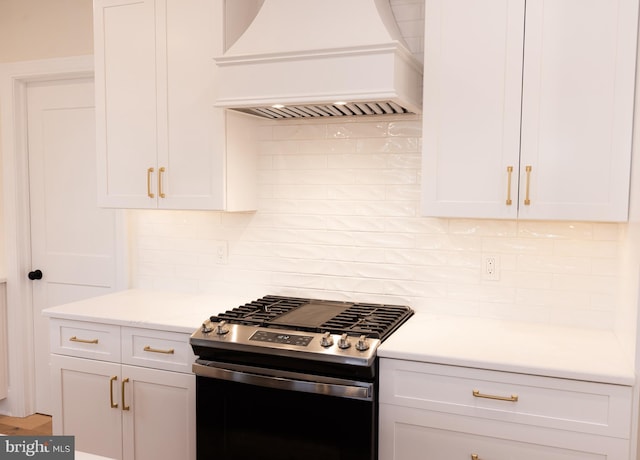 kitchen featuring stainless steel gas range oven, light stone counters, custom range hood, decorative backsplash, and white cabinets