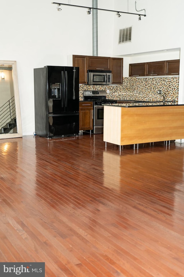 kitchen with a high ceiling, appliances with stainless steel finishes, dark hardwood / wood-style floors, and backsplash