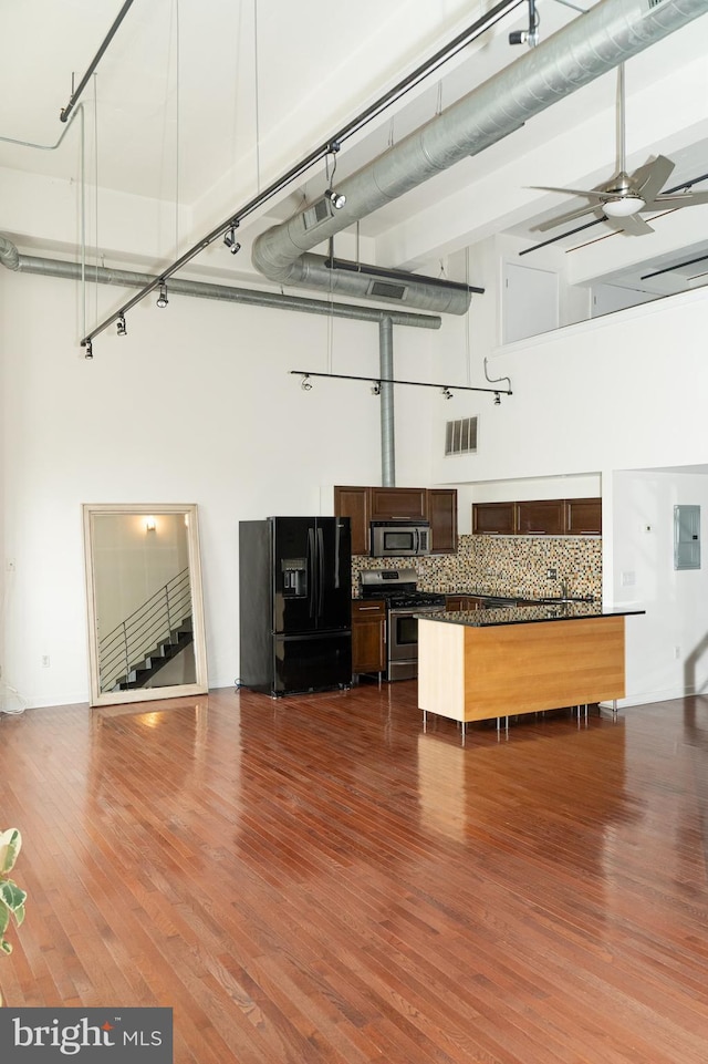 kitchen featuring ceiling fan, appliances with stainless steel finishes, a high ceiling, tasteful backsplash, and wood-type flooring