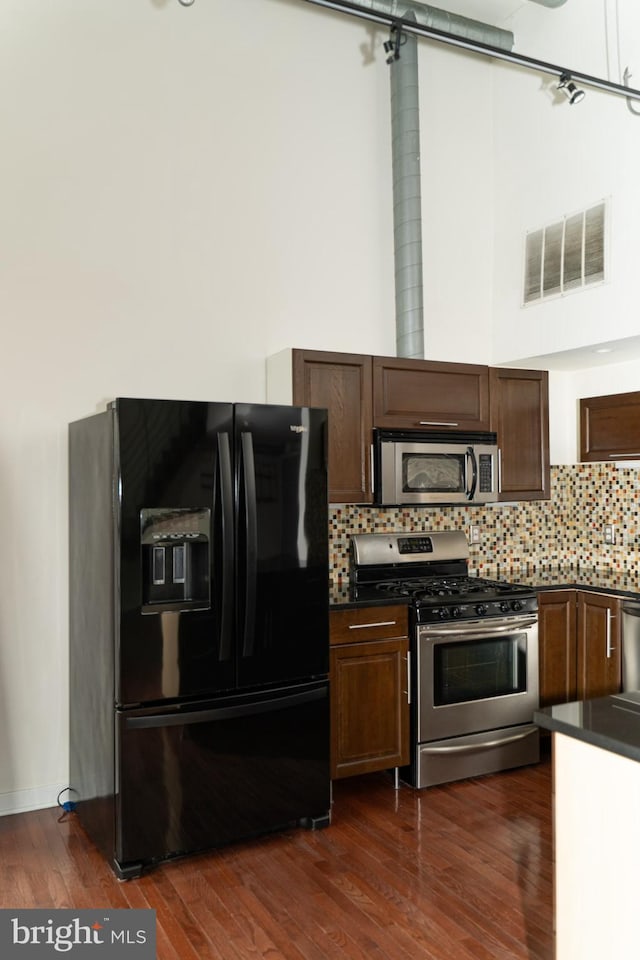 kitchen with stainless steel appliances, dark brown cabinets, dark hardwood / wood-style floors, and decorative backsplash