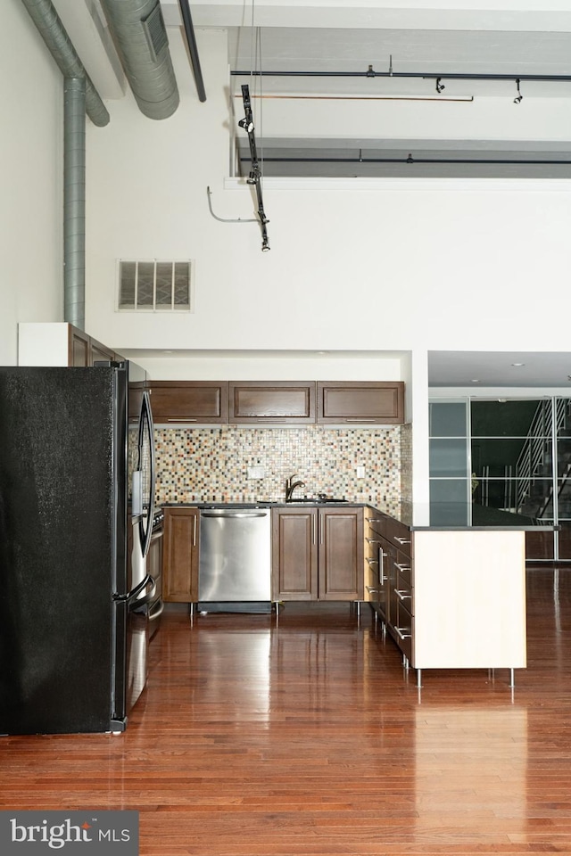 kitchen with dishwasher, black fridge, dark wood-type flooring, and backsplash