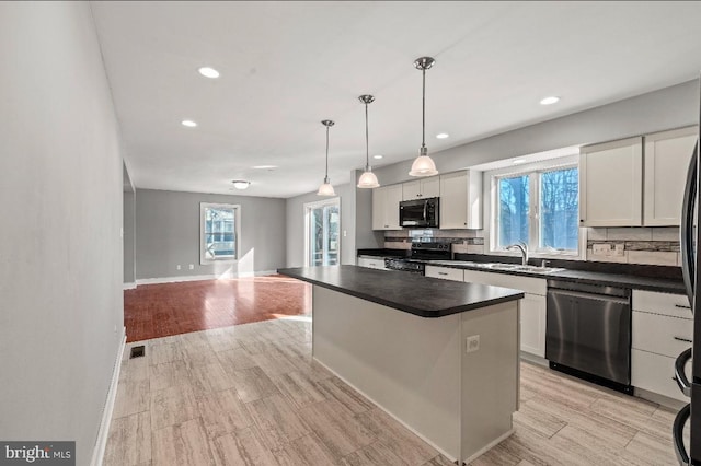 kitchen featuring appliances with stainless steel finishes, white cabinetry, hanging light fixtures, a center island, and decorative backsplash