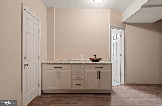 bar featuring light stone counters, sink, and dark hardwood / wood-style flooring