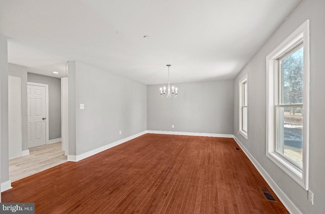 empty room with wood-type flooring and a chandelier