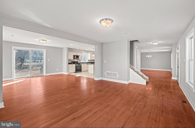 unfurnished living room featuring an inviting chandelier and light hardwood / wood-style flooring