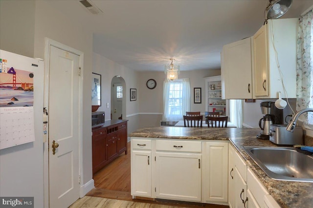 kitchen featuring white cabinetry, sink, hanging light fixtures, kitchen peninsula, and light wood-type flooring