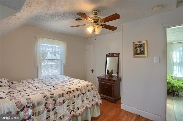 bedroom with multiple windows, vaulted ceiling, a textured ceiling, and light hardwood / wood-style flooring