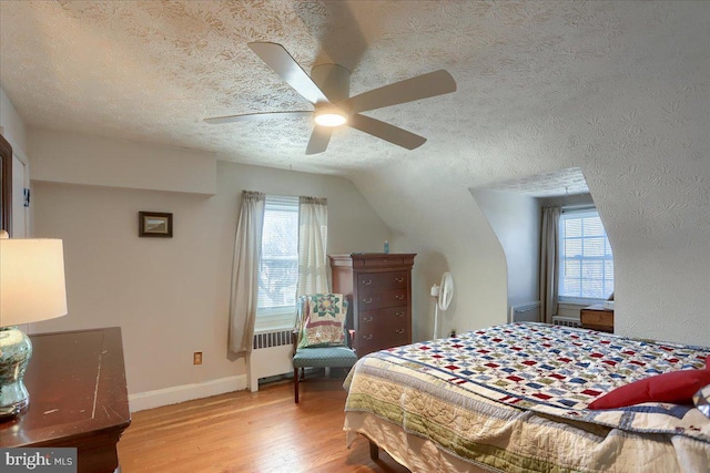 bedroom with ceiling fan, radiator heating unit, a textured ceiling, vaulted ceiling, and light wood-type flooring