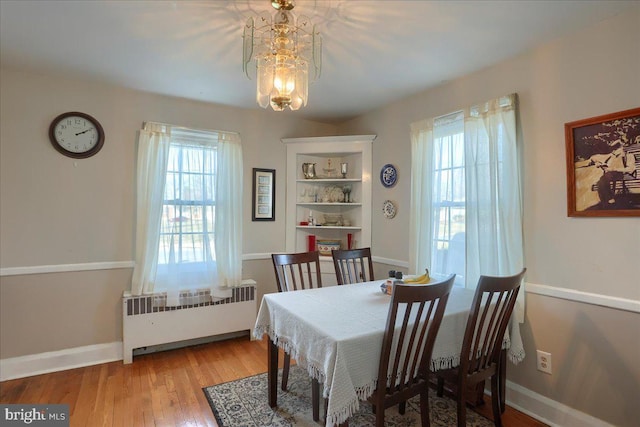 dining area with hardwood / wood-style floors, a healthy amount of sunlight, radiator heating unit, and a notable chandelier