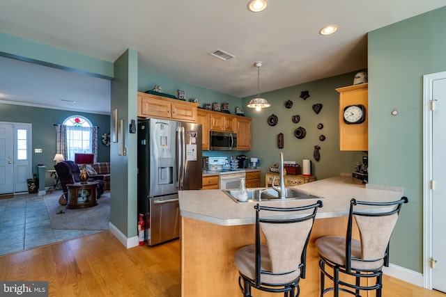 kitchen featuring a kitchen bar, sink, kitchen peninsula, stainless steel appliances, and light hardwood / wood-style floors