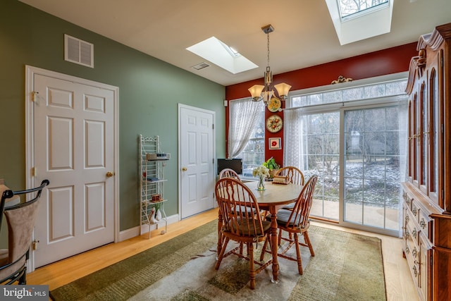 dining room featuring vaulted ceiling with skylight, a notable chandelier, and light hardwood / wood-style flooring