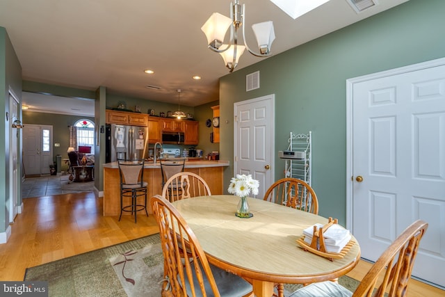 dining room with sink, a skylight, light hardwood / wood-style floors, and a notable chandelier