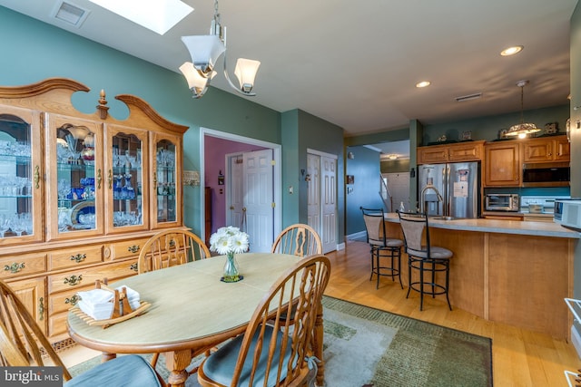 dining area with light hardwood / wood-style flooring, a chandelier, and a skylight