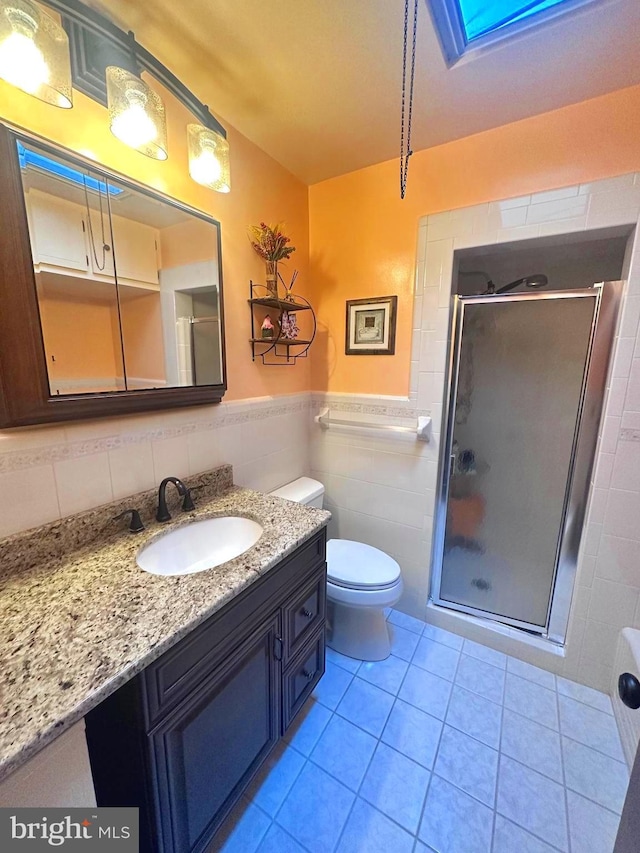 bathroom featuring toilet, a shower with shower door, tile walls, vanity, and tile patterned flooring